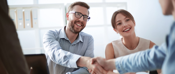 Two professionals in a business meeting smiling and shaking hands, with a bright office background, conveying a positive partnership in the workplace.